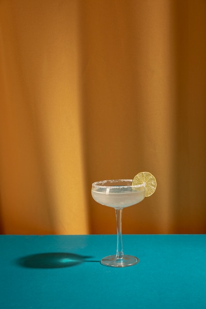 Het glas Margarita-cocktail versiert met kalk op blauwe lijst tegen geel gordijn
