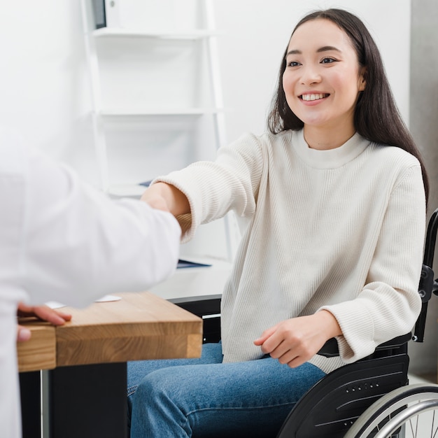 Gratis foto het glimlachen portret van een gehandicapte jonge vrouwenzitting op rolstoel het schudden handen met een persoon op het werk