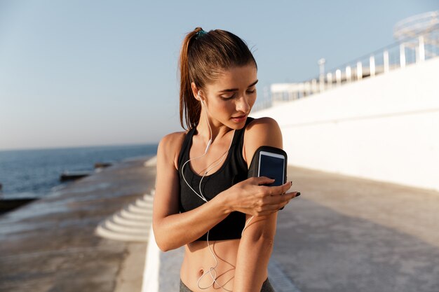 Het glimlachen van jonge het luisteren van de sportenvrouw muziek die mobiele telefoon met behulp van.