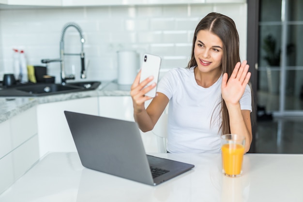 Het glimlachen van jonge vrouwenvideo die telefoon in keuken uitnodigen