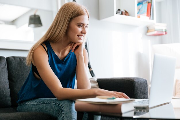 Het glimlachen van jonge vrouwenzitting en thuis het werken met laptop