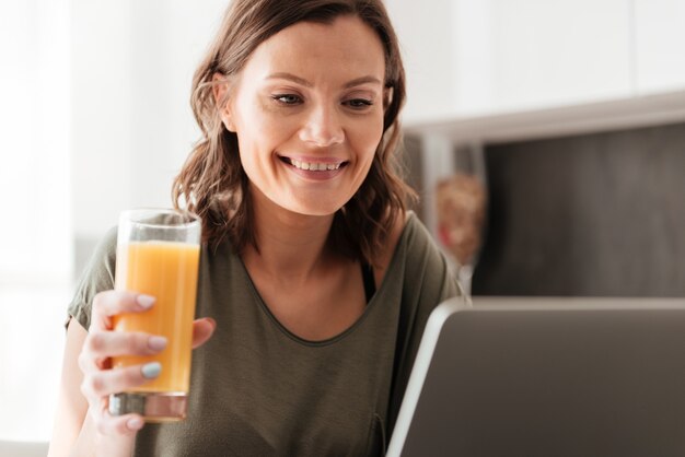 Het glimlachen van toevallig vrouw het drinken sap en het gebruiken van tabletcomputer op keuken