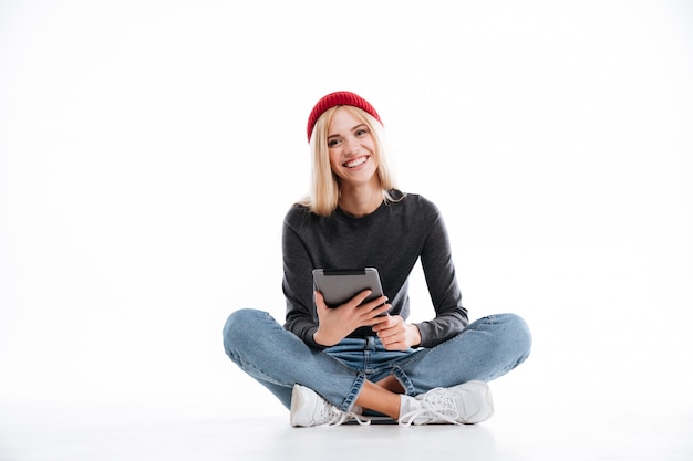 Het glimlachen vrouwenzitting op de vloer en het gebruiken van tabletcomputer