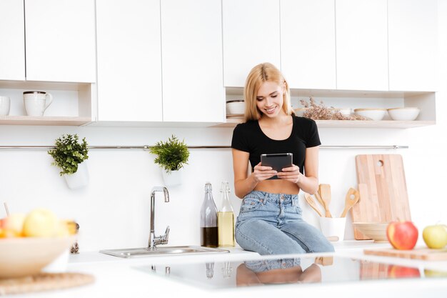 Het glimlachen vrouwenzitting op lijst en het gebruiken van tablet