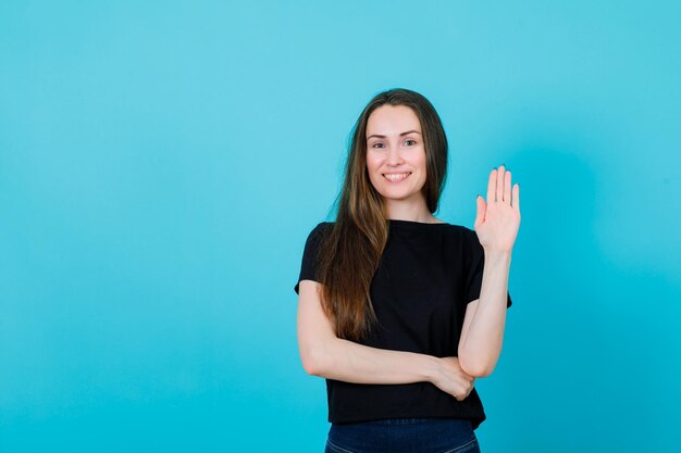 Het glimlachende jonge meisje toont handvol door hand op blauwe achtergrond op te heffen