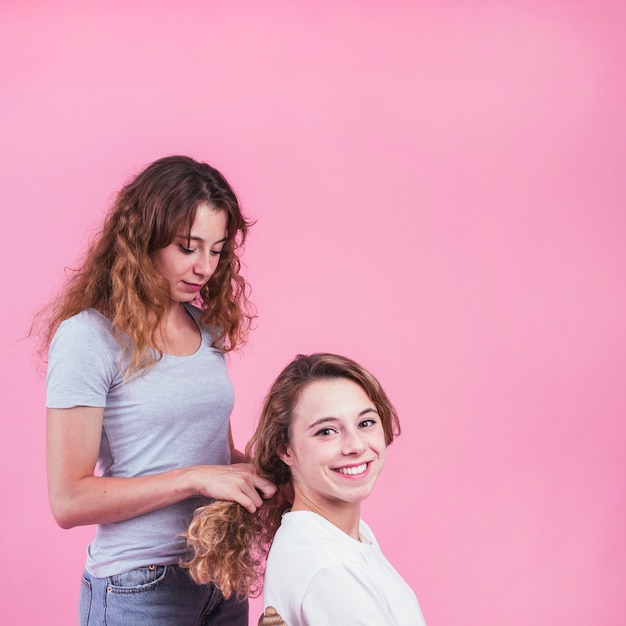 Het haar van vrouwelijke vlechten glimlachend vriend tegen roze achtergrond