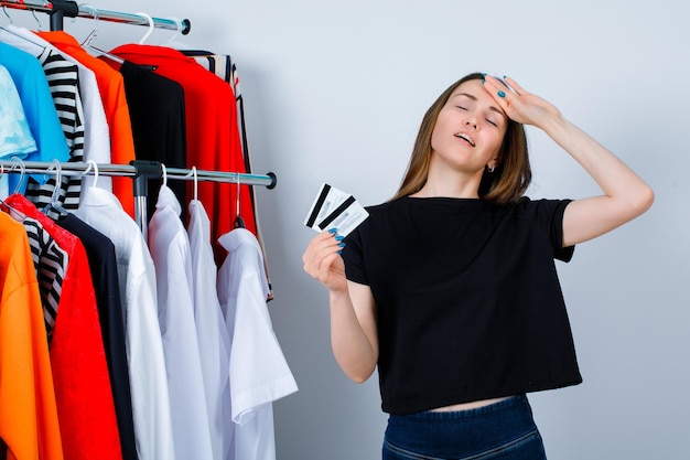 Het houden van creditcardsmeisje legt hand op voorhoofd op kledingachtergrond
