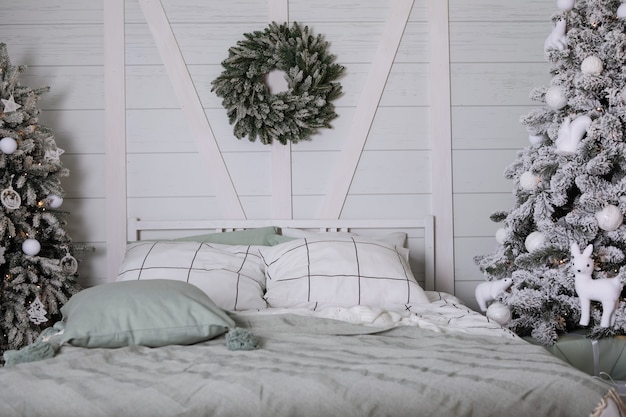 Het interieur van de slaapkamer met een bed met kussens, kerstbomen, een krans in een hoofdeinde in grijze tonaliteit.