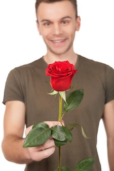 Het is voor jou! knappe jonge man die een rode roos uitrekt en glimlacht terwijl hij op een witte achtergrond staat