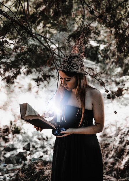 Gratis foto het jonge boek van de vrouwenlezing met het branden van kaars in bos