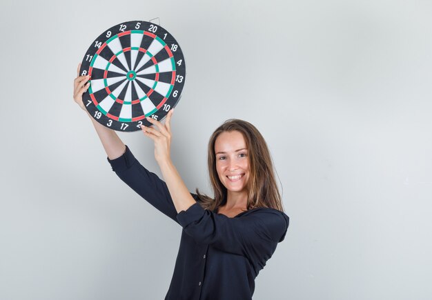 Het jonge dartbord van de vrouwenholding in zwart overhemd en op zoek vrolijk