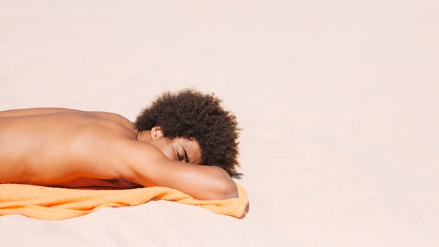 Gratis foto het jonge etnische mannetje zonnebaadt op zandig strand