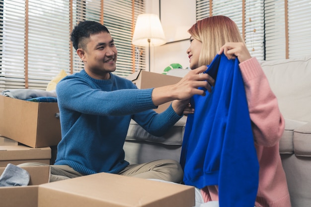 Het jonge gelukkige aziatische paar die zich aan hun nieuw huis bewegen, opent dozen om oude voorwerpen van oud huis te controleren