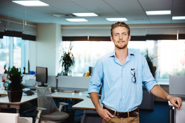 Het jonge knappe succesvolle zakenman glimlachen, die over bureau stelt