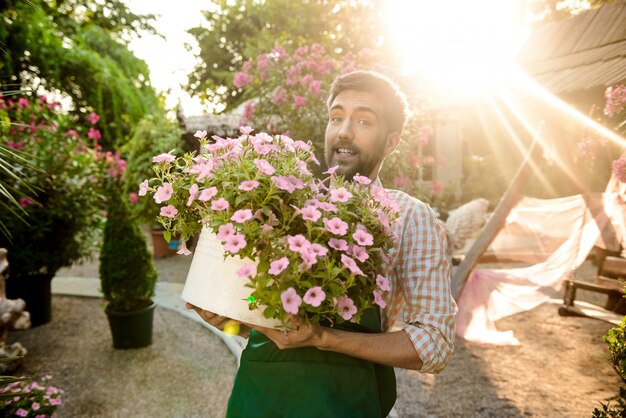Het jonge knappe tuinman glimlachen, die grote pot met bloemen houdt