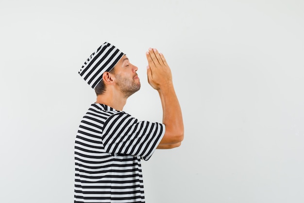 Het jonge mannetje dient biddend gebaar in gestreepte t-shirthoed in en kijkt hoopvol