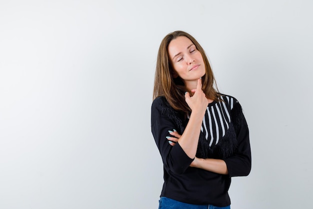 Het jonge meisje denkt door haar wijsvinger onder de kaak op een witte achtergrond te plaatsen