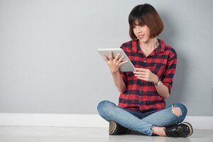 Het jonge meisje gezeten in lotusbloem stelt het doorbladeren van het net op haar digitale tablet-pc