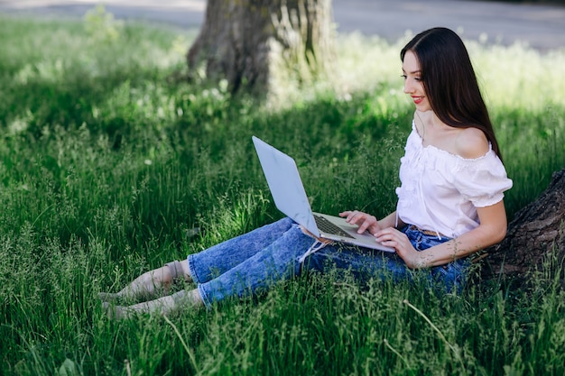 Het jonge meisje glimlachen, zittend op het gras met een laptop op haar benen