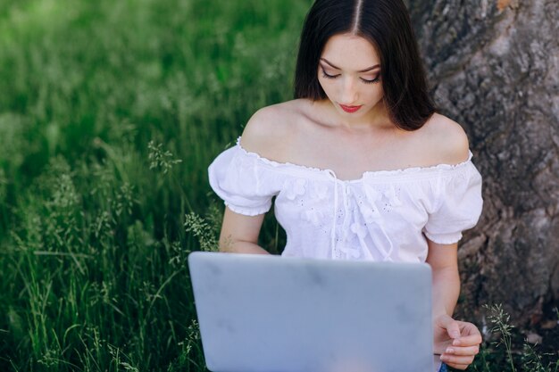 Het jonge meisje glimlachen, zittend op het gras met een laptop