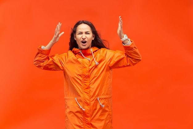 Het jonge meisje poseren in studio in herfst jas geïsoleerd op rood. Menselijke negatieve emoties.