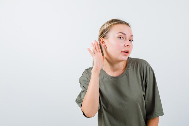 Het jonge meisje probeert te luisteren door haar hand achter het oor op een witte achtergrond te houden