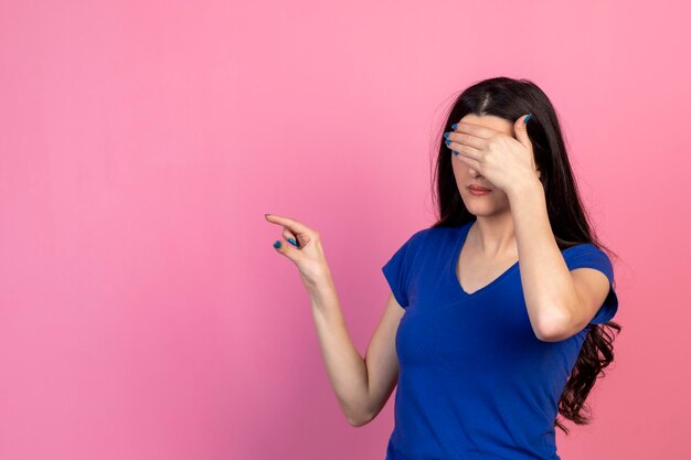 Het jonge meisje sluit haar ogen met haar hand en wijst met de vinger naar rechts