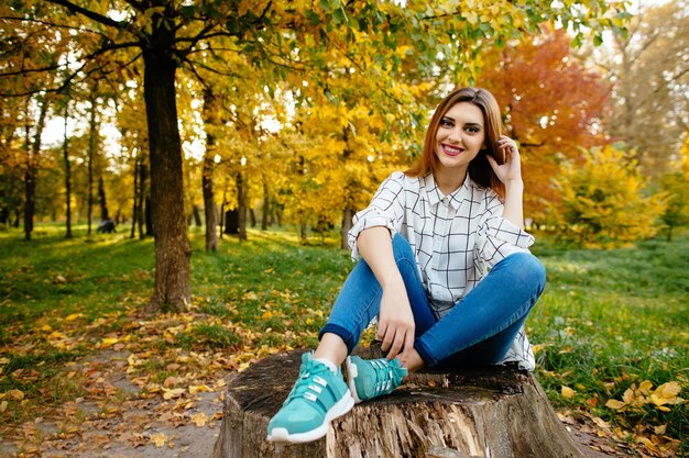 Het jonge meisje zit op een stomp in het de herfstpark.