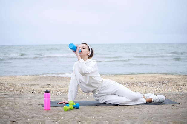 Het jonge mooie meisje dat op de yogamat ligt en water drinkt foto van hoge kwaliteit