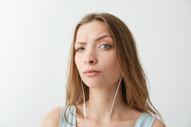 Het jonge mooie meisje heft brow op luisterend aan stromende muziek in hoofdtelefoons.