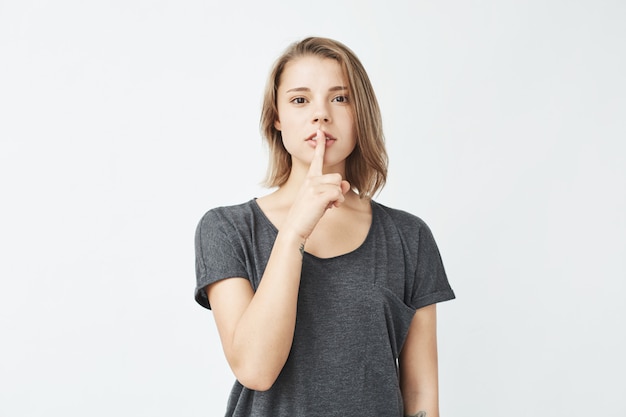 Gratis foto het jonge mooie meisje in het grijze t-shirt tonen houdt zwijgen.