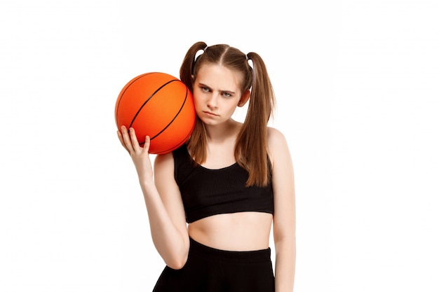 Het jonge mooie meisje stellen met basketbal, dat op witte muur wordt geïsoleerd