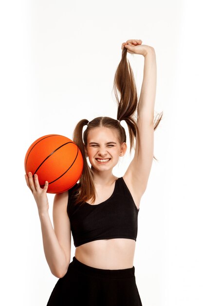 Het jonge mooie meisje stellen met basketbal, dat op witte muur wordt geïsoleerd