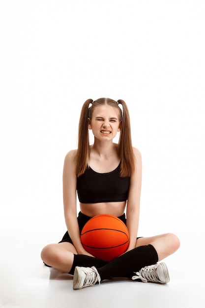 Gratis foto het jonge mooie meisje stellen met basketbal over witte muur