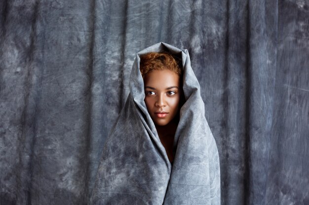 Het jonge mooie vrouw stellen, die zich in grijze doek verpakken