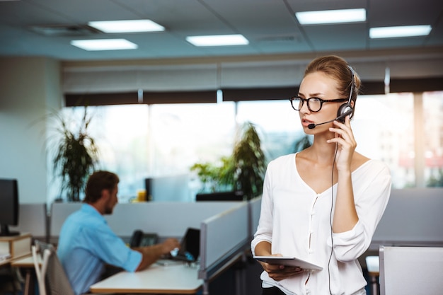 Het jonge mooie vrouwelijke exploitant van de steuntelefoon spreken, die over bureau raadplegen