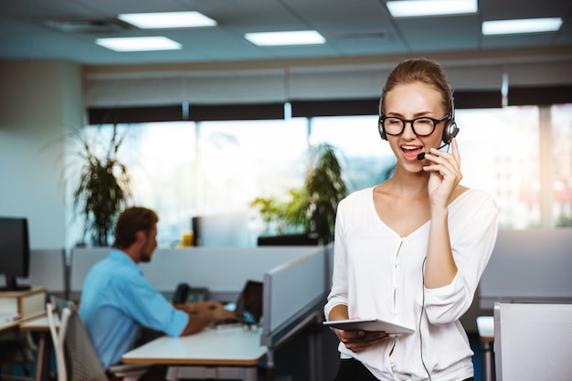 Het jonge mooie vrouwelijke exploitant van de steuntelefoon spreken, die over bureau raadplegen