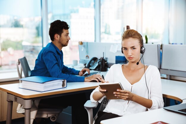 Het jonge mooie vrouwelijke exploitant van de steuntelefoon spreken, die over bureau raadplegen