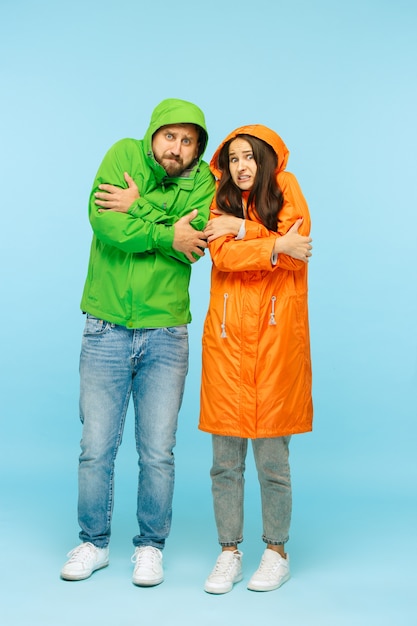 Het jonge paar poseren in de studio in herfst jas geïsoleerd op blauw. Menselijke negatieve emoties. Concept van het koude weer. Vrouwelijke en mannelijke modeconcepten