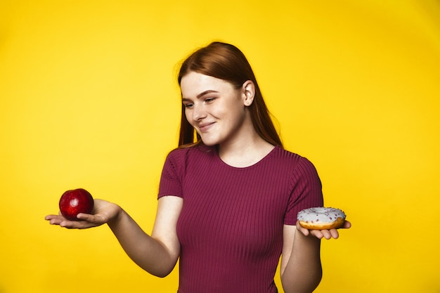 Het jonge roodharigemeisje kiest tussen een appel en een doughnut