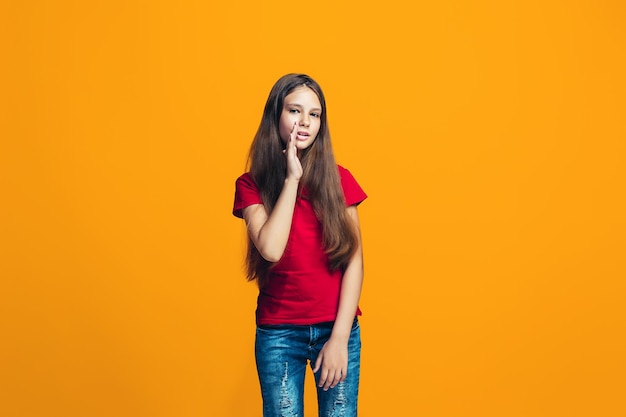 Het jonge tienermeisje dat een geheim achter haar fluistert overhandigt oranje achtergrond