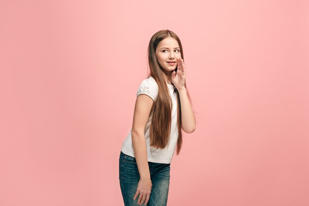 Het jonge tienermeisje fluistert een geheim achter haar hand over roze muur