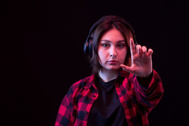 Het jonge vrouw stellen met geruit rood en zwart overhemd gebruikend hoofdtelefoons