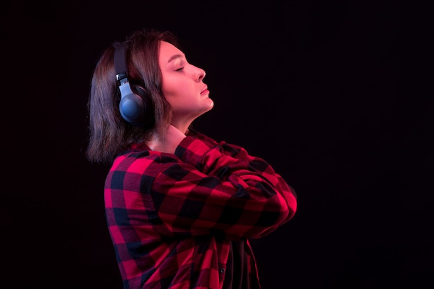 Het jonge vrouw stellen met geruit rood en zwart overhemd gebruikend hoofdtelefoons