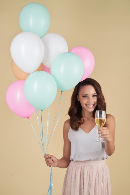 Het Kaukasische vrouw stellen in studio met bos van heliumballons en champagne