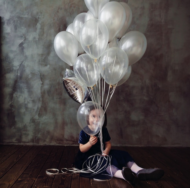 Het kleine meisje zit op de grond en houdt de ballonnen in de kamer