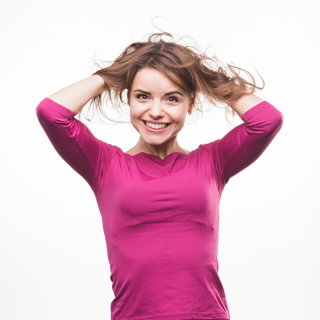 Het leuke het glimlachen jonge vrouw spelen met haar haren tegen witte achtergrond