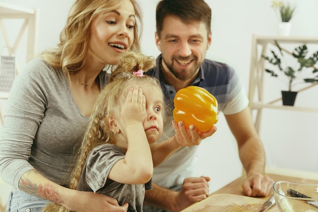 Het leuke kleine meisje en haar mooie ouders snijden groenten