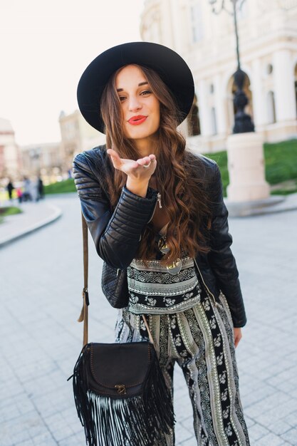 Het levensstijlportret van vrij vrolijke vrouw verzendt kus, lachend, genietend van vakantie in oude Europese stad. Street fashion look. Stijlvolle lente-outfit.