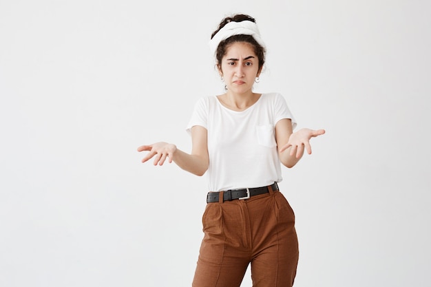 Het maakt niet uit. Clueless donkerharige vrouw gekleed in een wit T-shirt, lippen opjagend, schouders ophalend, starend van woede nadat ze iets verkeerds had gedaan maar zich niet schuldig voelde